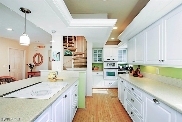 kitchen featuring white appliances, light wood-type flooring, white cabinetry, a raised ceiling, and decorative light fixtures