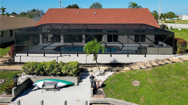 rear view of house featuring glass enclosure, a fenced in pool, a yard, and a patio