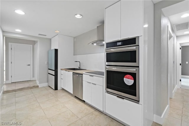 kitchen featuring white cabinetry, sink, wall chimney range hood, light tile patterned floors, and appliances with stainless steel finishes