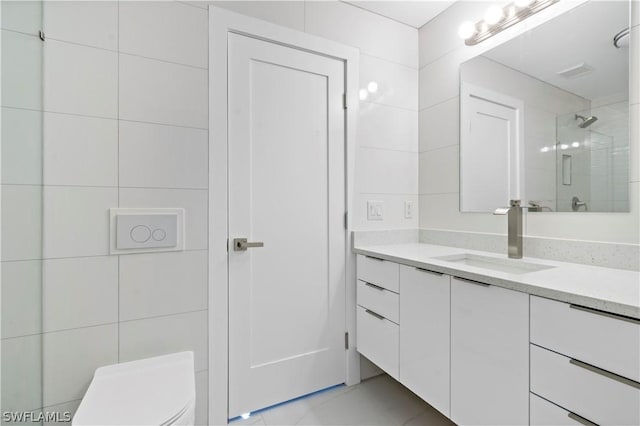 bathroom with a tile shower, tile patterned flooring, toilet, vanity, and tile walls