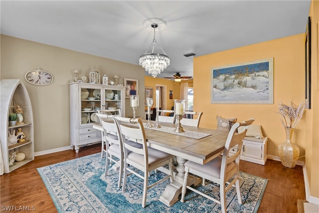 dining room with ceiling fan with notable chandelier and dark wood-type flooring