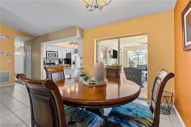 dining room with ceiling fan with notable chandelier, lofted ceiling, and light tile patterned floors