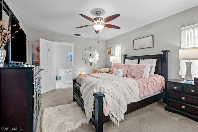 bedroom with ensuite bathroom, light carpet, and ceiling fan