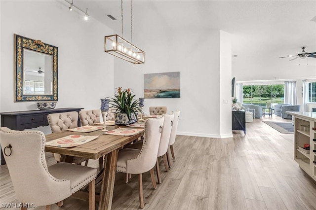 dining area featuring rail lighting, high vaulted ceiling, light hardwood / wood-style floors, and ceiling fan with notable chandelier