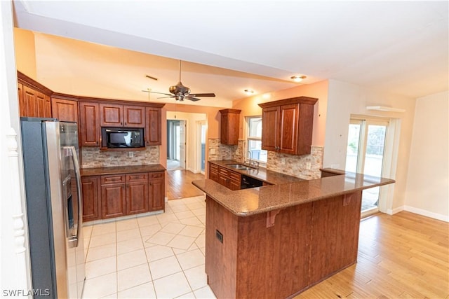 kitchen featuring kitchen peninsula, a kitchen bar, sink, black appliances, and light hardwood / wood-style floors