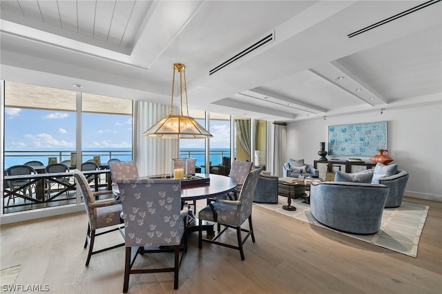 dining area with floor to ceiling windows, light hardwood / wood-style flooring, a raised ceiling, and a water view