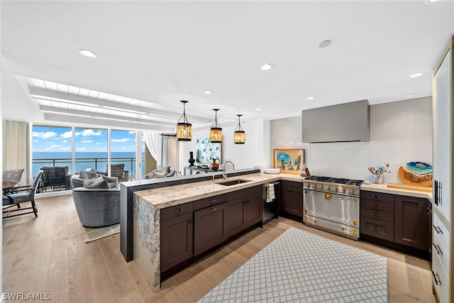 kitchen with kitchen peninsula, high end stainless steel range oven, light hardwood / wood-style floors, wall chimney exhaust hood, and sink