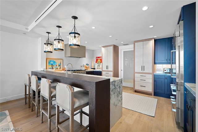 kitchen featuring blue cabinets, a kitchen breakfast bar, light hardwood / wood-style flooring, kitchen peninsula, and pendant lighting