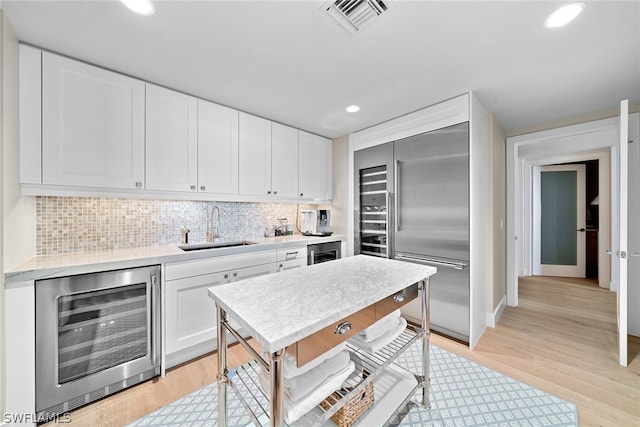 kitchen featuring wine cooler, sink, white cabinets, light wood-type flooring, and built in fridge