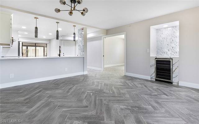 unfurnished living room with parquet flooring, wine cooler, a fireplace, and an inviting chandelier