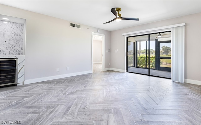 unfurnished room featuring a fireplace, ceiling fan, beverage cooler, and light parquet flooring