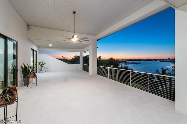 patio terrace at dusk featuring ceiling fan and a water view