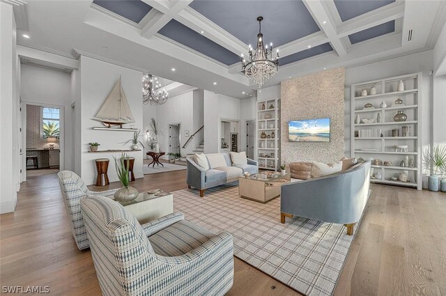 living room featuring a towering ceiling, ornamental molding, coffered ceiling, an inviting chandelier, and light hardwood / wood-style floors