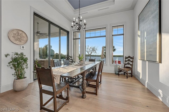 dining room featuring a raised ceiling, crown molding, a healthy amount of sunlight, and light wood-type flooring