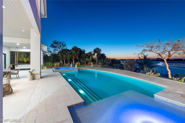 pool at dusk featuring a patio area and an in ground hot tub