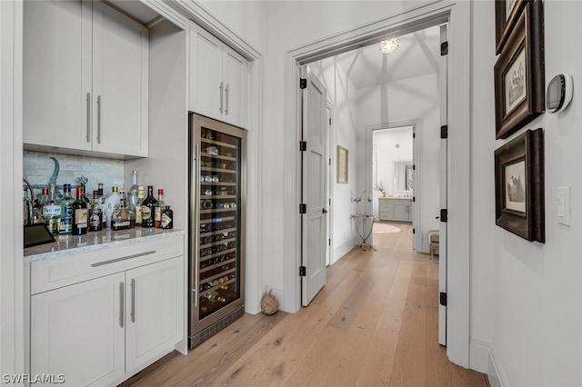 interior space with backsplash, light stone counters, beverage cooler, light hardwood / wood-style floors, and white cabinetry