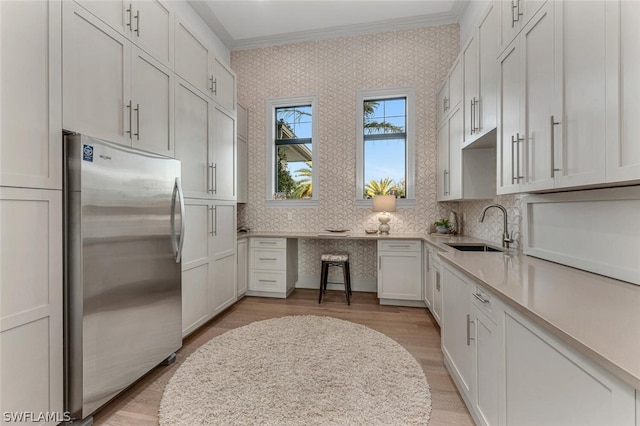 kitchen with stainless steel fridge, white cabinetry, crown molding, and sink