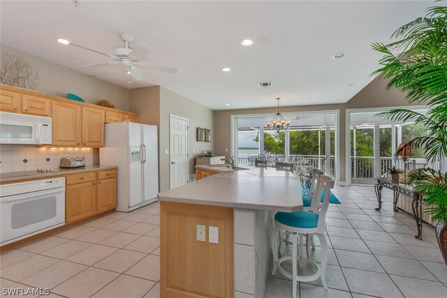 kitchen with white appliances, a center island with sink, pendant lighting, ceiling fan with notable chandelier, and backsplash