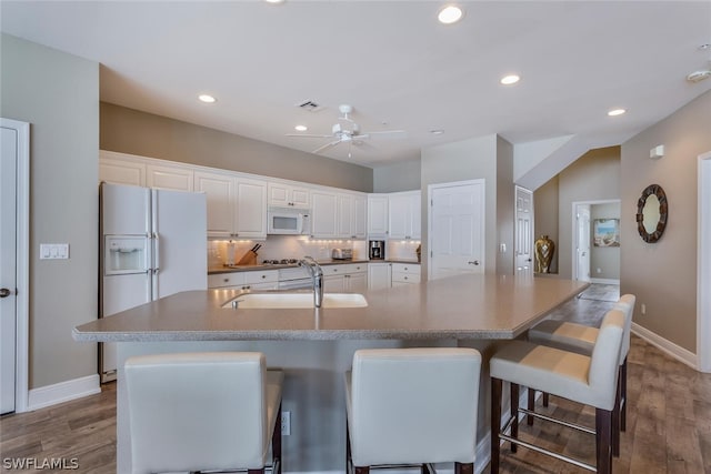 kitchen with a large island with sink, white cabinetry, hardwood / wood-style flooring, and white appliances