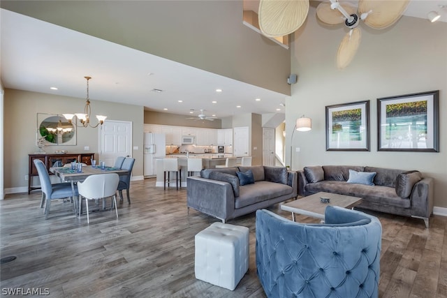 living room featuring a towering ceiling, ceiling fan with notable chandelier, and hardwood / wood-style floors