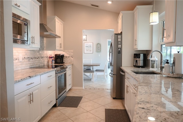 kitchen with appliances with stainless steel finishes, wall chimney exhaust hood, white cabinetry, lofted ceiling, and pendant lighting