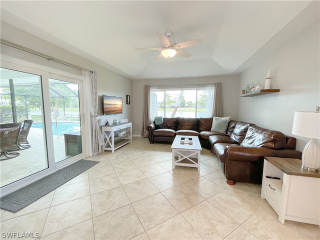 living room featuring a raised ceiling, ceiling fan, and light tile floors