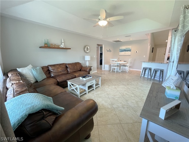 tiled living room with ceiling fan and a raised ceiling