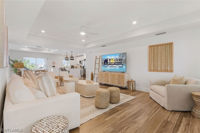 living room with light hardwood / wood-style flooring, ceiling fan, and a tray ceiling