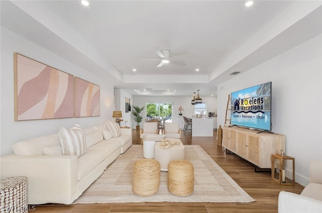 living room with hardwood / wood-style flooring, ceiling fan, and a raised ceiling