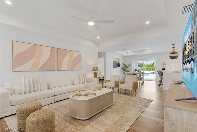 living room with a raised ceiling, light hardwood / wood-style floors, and ceiling fan