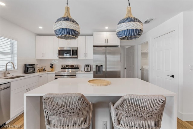 kitchen with white cabinetry, stainless steel appliances, sink, a kitchen island, and light hardwood / wood-style floors