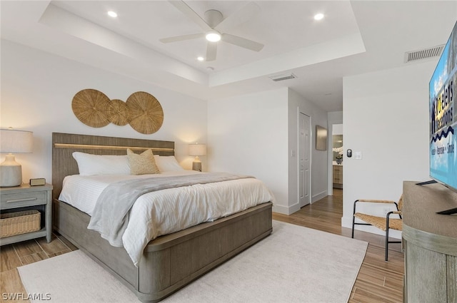 bedroom featuring a closet, ceiling fan, light hardwood / wood-style floors, and a tray ceiling