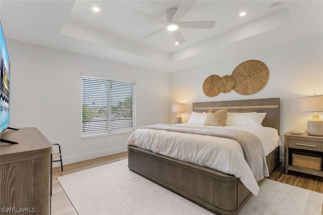 bedroom with wood-type flooring, ceiling fan, and a tray ceiling