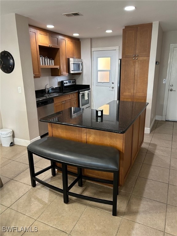 kitchen featuring a kitchen bar, sink, dark stone counters, a kitchen island, and stainless steel appliances