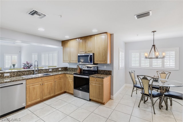 kitchen featuring an inviting chandelier, stainless steel appliances, dark stone counters, and sink