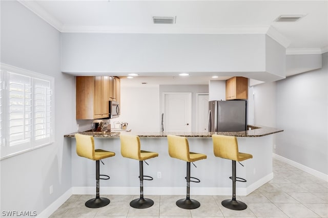 kitchen with kitchen peninsula, appliances with stainless steel finishes, dark stone countertops, and a breakfast bar area