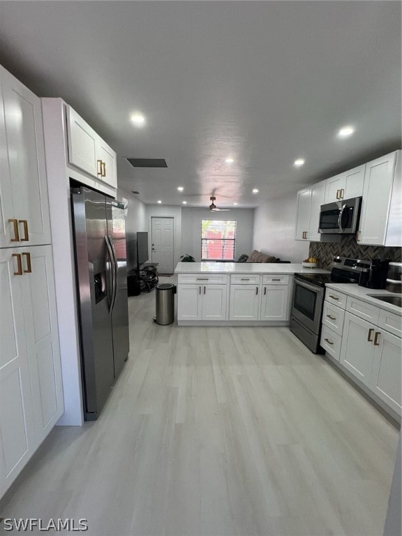 kitchen with light wood-type flooring, kitchen peninsula, white cabinets, ceiling fan, and appliances with stainless steel finishes