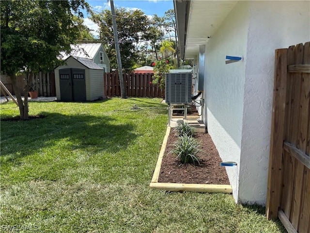 view of yard featuring an outbuilding, a fenced backyard, central AC unit, and a storage unit