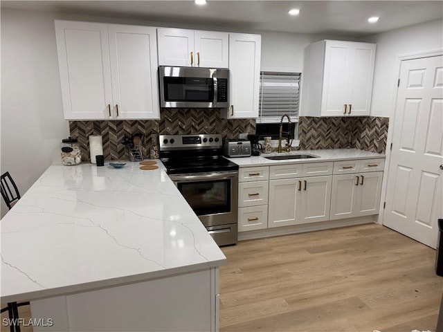 kitchen with light stone counters, a sink, white cabinets, light wood-style floors, and appliances with stainless steel finishes