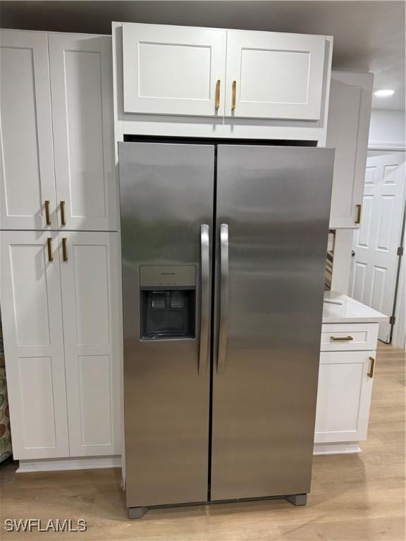 kitchen with light wood-style floors, light countertops, white cabinets, and stainless steel fridge