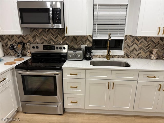 kitchen featuring white cabinets, decorative backsplash, light stone countertops, stainless steel appliances, and a sink