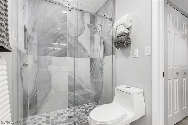 bathroom featuring a shower with door and toilet