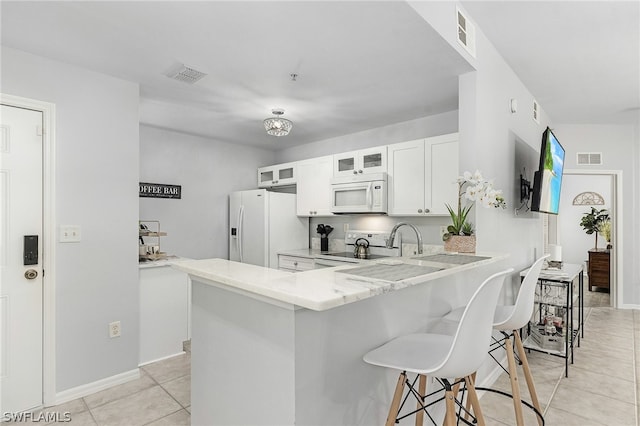 kitchen featuring white cabinets, light tile patterned flooring, kitchen peninsula, white appliances, and a breakfast bar