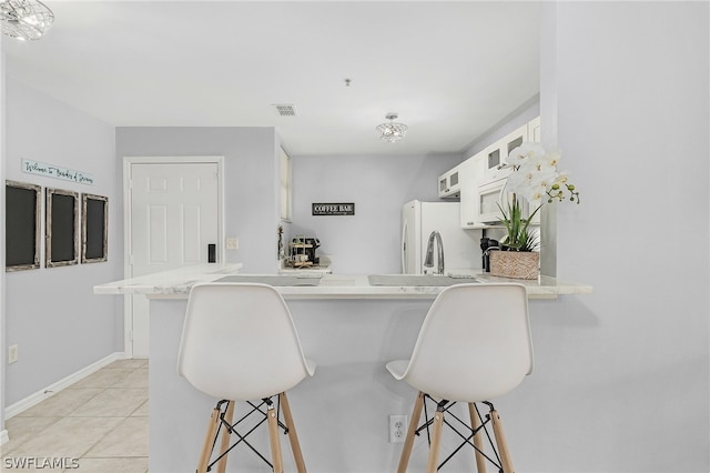 kitchen with white refrigerator, white cabinetry, kitchen peninsula, and a breakfast bar area