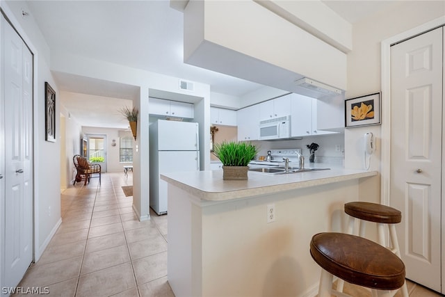 kitchen featuring kitchen peninsula, a breakfast bar area, white appliances, light tile flooring, and white cabinetry