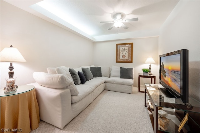 carpeted living room with a raised ceiling and ceiling fan