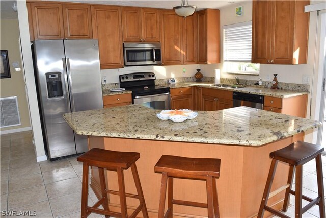 kitchen featuring light tile flooring, appliances with stainless steel finishes, sink, a breakfast bar area, and a kitchen island