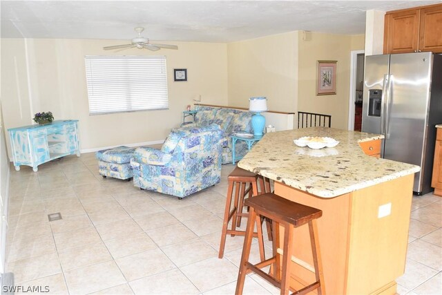 kitchen with a center island, light stone countertops, light tile floors, stainless steel fridge, and ceiling fan