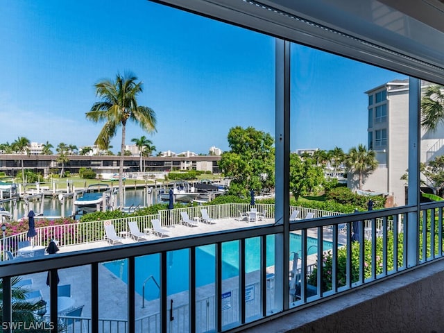 balcony with a water view, a boat dock, and a community pool