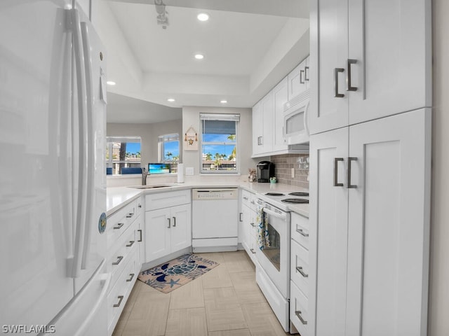 kitchen with white cabinets, white appliances, a tray ceiling, sink, and tasteful backsplash